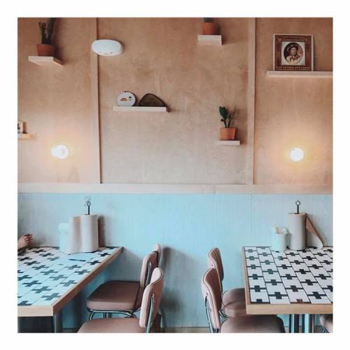 Cozy café interior with wooden walls, potted plants, and patterned tables, featuring soft lighting and minimalist decor.