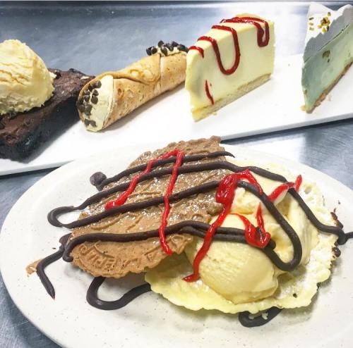 A plate with two scoops of ice cream on a waffle, drizzled with chocolate and red sauce, alongside various desserts.