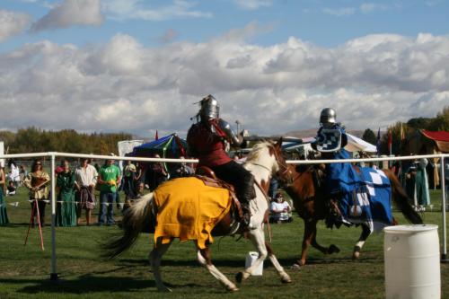 Two knights in armor on horseback compete in a jousting event, with spectators and tents in the background.