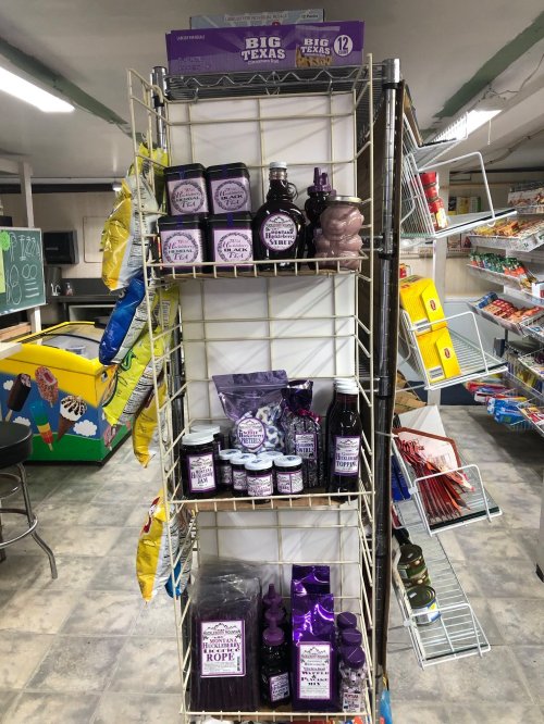 A display rack filled with various purple-themed products, including jars, bottles, and snacks in a store setting.