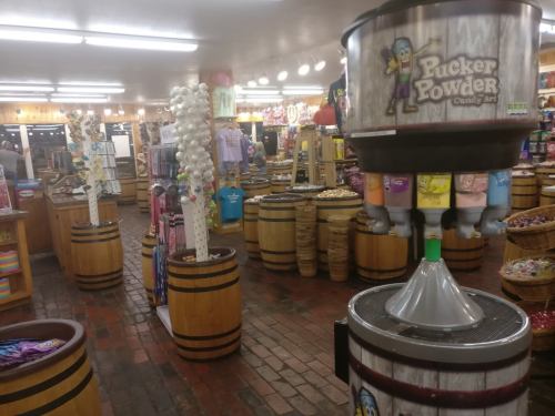 Interior of a candy store with colorful displays, barrels, and a Pucker Powder machine in the center.