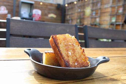 A cast iron dish holds two golden-brown slices of crispy bread on a wooden table outdoors.