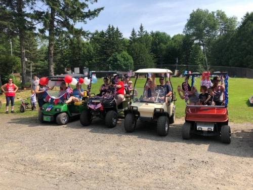 A group of people decorated golf carts with festive colors, celebrating outdoors in a park-like setting.