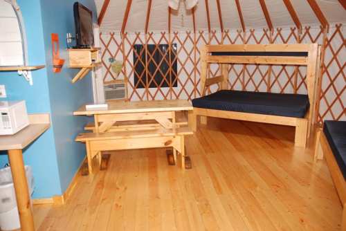 Interior of a yurt featuring wooden furniture, a table, bunk beds, and a TV mounted on the wall.