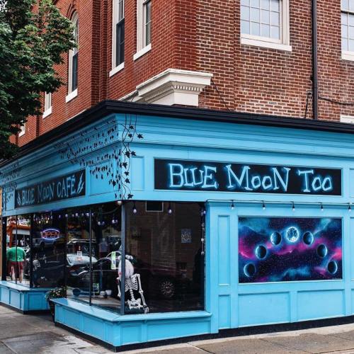 A vibrant blue cafe with a cosmic-themed mural and a skeleton decoration in the window, set in a brick building.