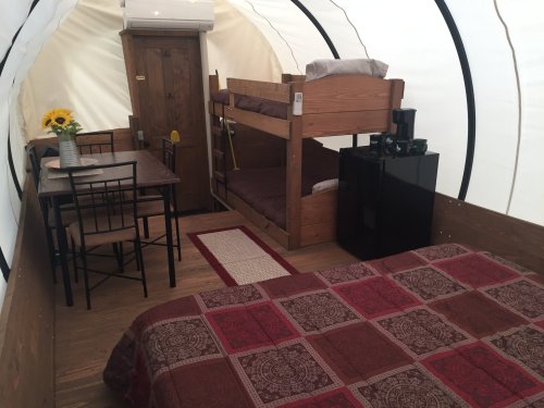 Cozy interior of a glamping tent featuring a double bed, bunk beds, dining table, and kitchenette. Sunflower centerpiece.