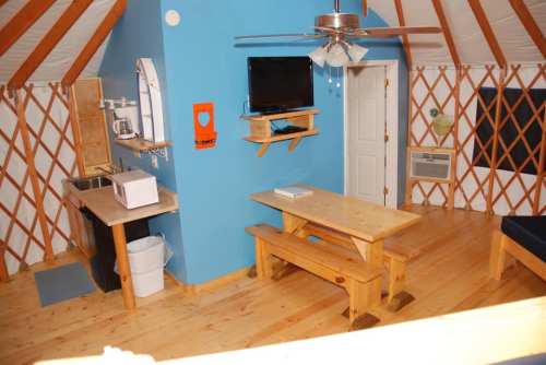 Interior of a cozy yurt featuring a blue wall, wooden furniture, a TV, and kitchen amenities.