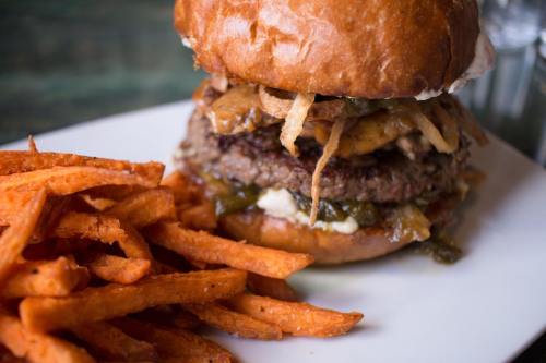 A juicy burger stacked with toppings, served with a side of crispy sweet potato fries on a white plate.
