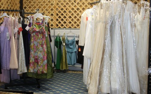 A display of various dresses, including formal gowns and casual wear, hanging on racks in a boutique setting.
