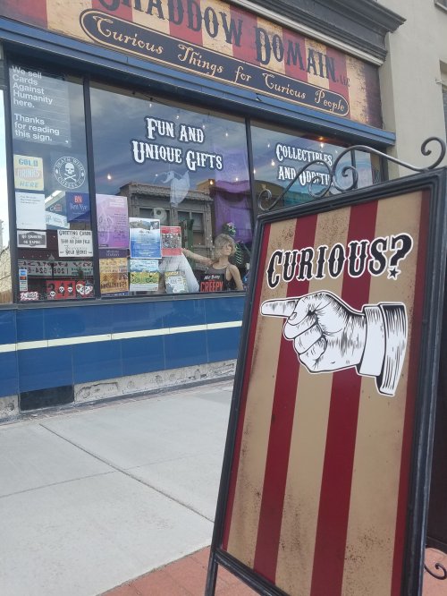 A storefront with a sign reading "CURIOUS?" and a window displaying various unique gifts and collectibles.