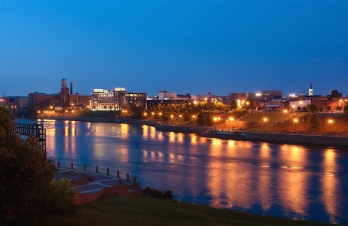 A serene river scene at dusk, reflecting city lights and buildings along the waterfront.