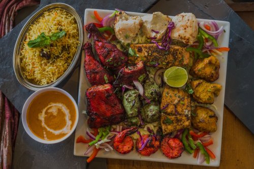 A vibrant platter of assorted grilled meats, seafood, and vegetables, served with rice and a side of sauce.