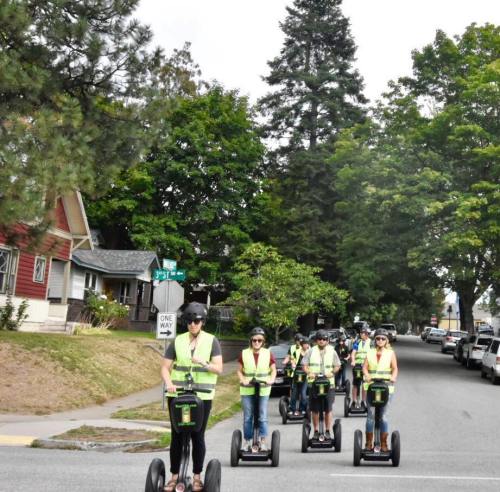 A group of people in safety vests riding segways down a tree-lined street.