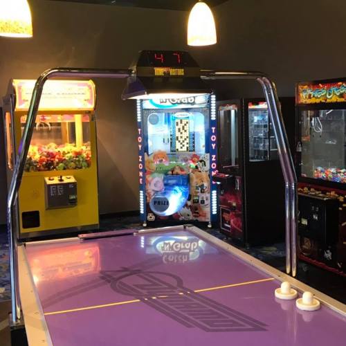 A purple air hockey table with a score display, surrounded by arcade games in a brightly lit game room.