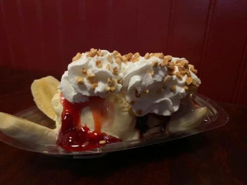 A banana split topped with whipped cream, nuts, and strawberry sauce, served in a clear dish.