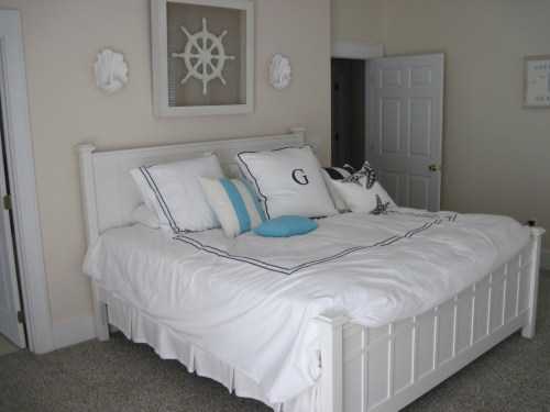 A cozy bedroom featuring a white bed with decorative pillows, light walls, and nautical-themed decor.