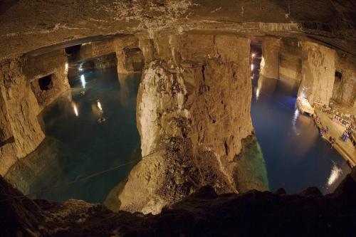A vast underground cavern with water, illuminated by lights, showcasing rocky formations and a serene atmosphere.