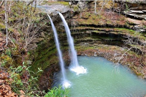 A serene waterfall cascading into a turquoise pool, surrounded by lush greenery and rocky cliffs.