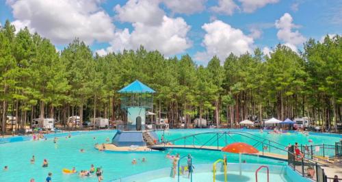 A vibrant swimming pool surrounded by trees, with people enjoying the water and a diving platform in the center.