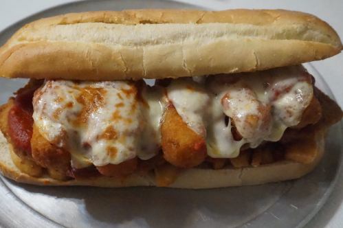 A hearty sandwich filled with breaded chicken, marinara sauce, and melted cheese, served in a soft hoagie roll.