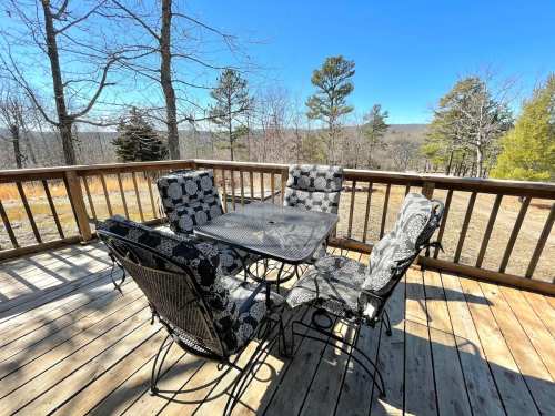 A wooden deck with a black and white patterned table and chairs, surrounded by trees and a clear blue sky.