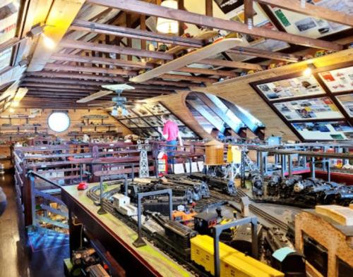 A spacious attic filled with model trains, displays, and memorabilia, with a person examining the collection.