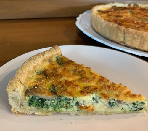 A slice of spinach quiche on a white plate, showcasing a golden crust and green filling.