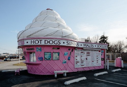 A whimsical ice cream stand shaped like a giant ice cream cone, featuring a menu of hot dogs, sundaes, and yogurt.