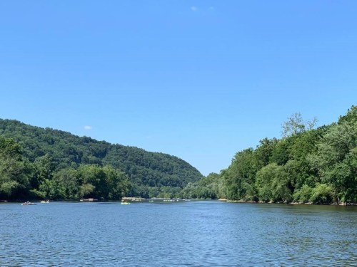 A serene river scene surrounded by lush green hills under a clear blue sky.