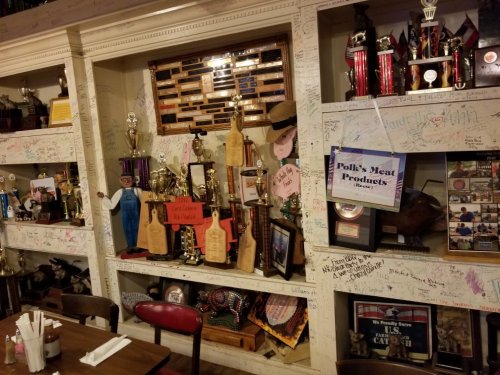 A wall display filled with trophies, memorabilia, and handwritten notes in a cozy restaurant setting.