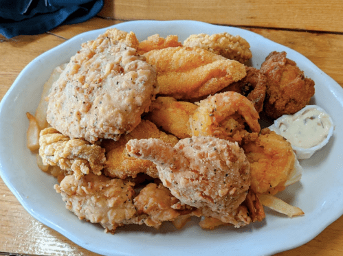 A platter of assorted fried seafood, including shrimp, fish, and hushpuppies, served with a side of dipping sauce.