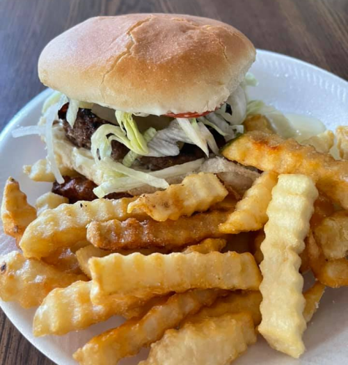 A plate with a hamburger topped with lettuce and pickles, accompanied by a serving of crinkle-cut fries.