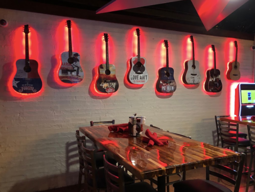 A dimly lit restaurant wall featuring illuminated guitars and a wooden table set for dining.