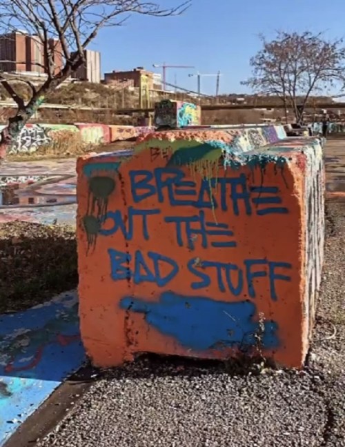 A colorful graffiti-covered concrete block with the phrase "Breathe out the bad stuff" painted on it.