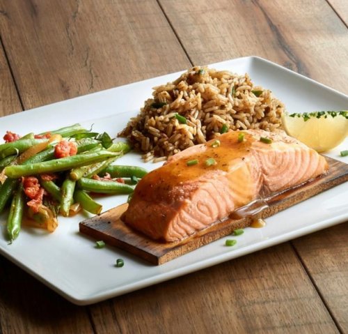 A plate featuring grilled salmon with a glaze, served with rice and sautéed green beans on a wooden board.