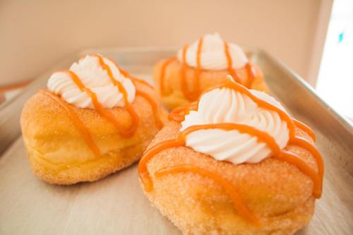 Three fluffy pastries topped with whipped cream and drizzled with caramel sauce, resting on a tray.