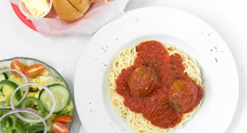 A plate of spaghetti with meatballs in marinara sauce, accompanied by a side salad and a bun.
