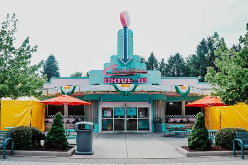 A retro-style drive-in restaurant with colorful umbrellas, outdoor seating, and a bright neon sign.