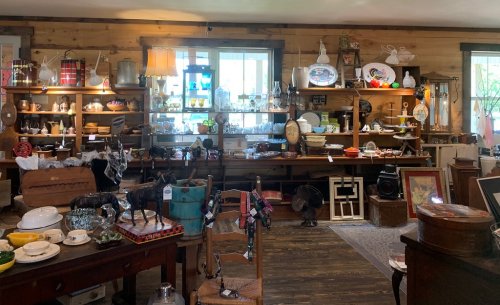A cozy antique shop filled with various vintage items, including dishes, decor, and furniture, arranged on wooden shelves.