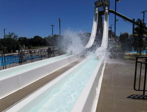 Two water slides with splashes as riders descend into a pool area on a sunny day.