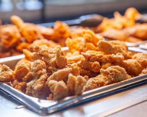 A close-up of golden, crispy fried chicken pieces in a serving tray, with more chicken in the background.