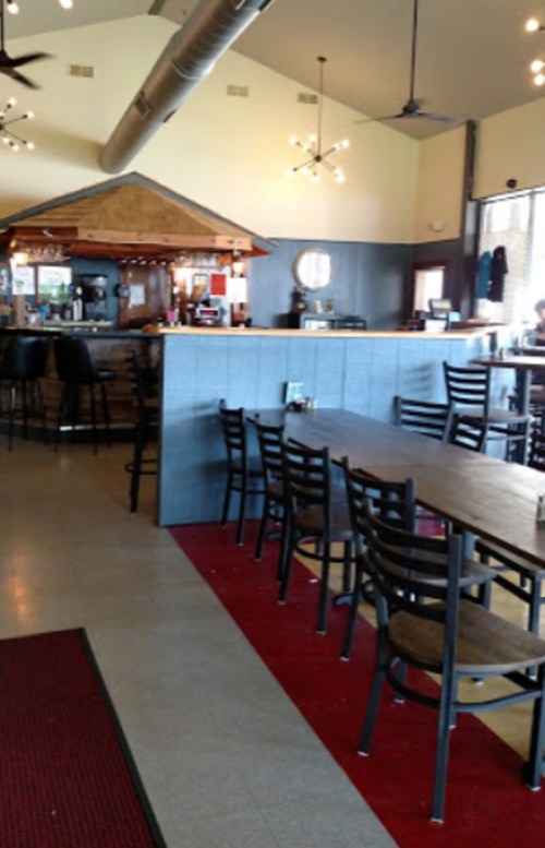 Interior of a restaurant featuring a bar area, tables, and chairs, with modern lighting and a warm atmosphere.