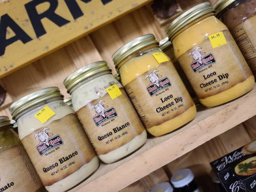 Jars of cheese dips labeled "Queso Blanco" and "Loco Cheese Dip" on a wooden shelf with price tags.