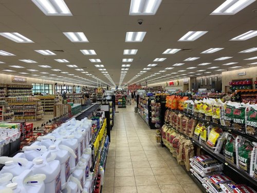 A wide aisle in a grocery store filled with shelves of various products and bright overhead lights.