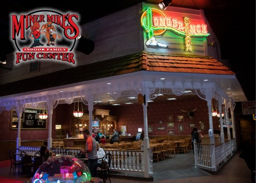 A brightly lit indoor fun center with a restaurant area, featuring a colorful sign and a cozy seating arrangement.