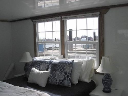 Cozy bedroom with a bed, decorative pillows, and large windows showing a city skyline in the background.