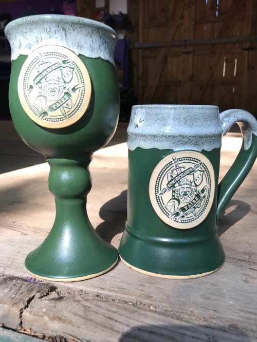 Two green ceramic drinkware pieces: a goblet and a mug, both featuring intricate designs on their surfaces.