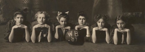 A vintage black-and-white photo of six young women posing with their arms crossed, resting on a basketball marked "W.B. '07."