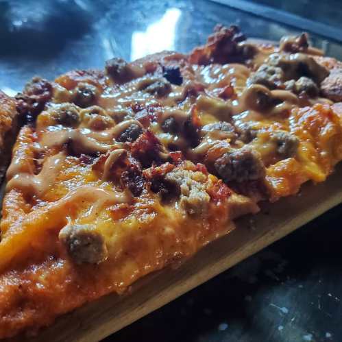 A close-up of a slice of pizza topped with melted cheese, sausage, and crispy edges on a wooden serving board.