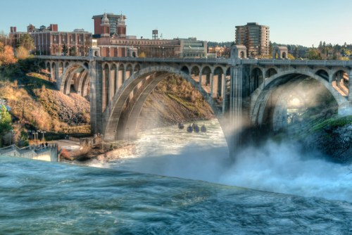 A scenic view of a large stone bridge over a river, with mist rising and buildings in the background.